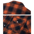 Close-up of orange and navy checked flannel fabric showing the collar seam and button-flap chest pocket detail