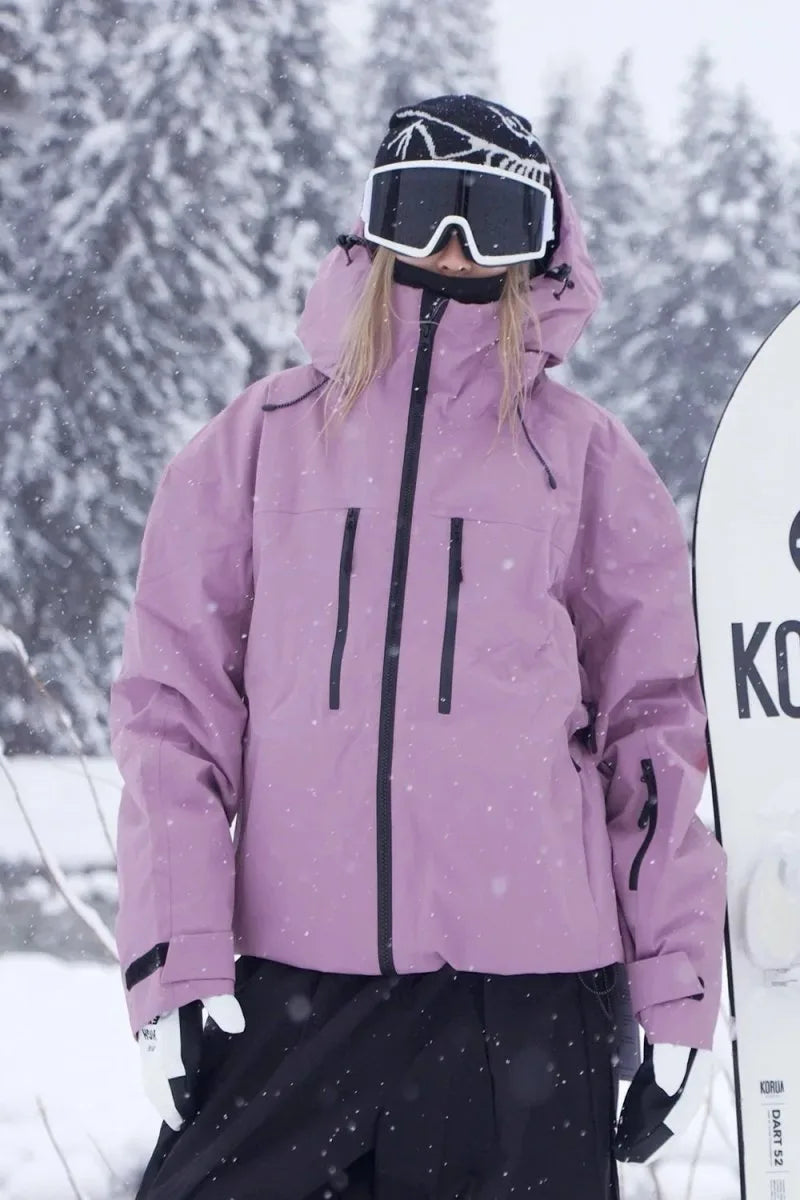 Close-up front detail of the dusky pink jacket showing zip chest pockets and storm hood, standing beside a snowboard