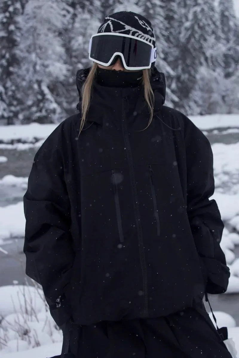 Close-up front view of the all black jacket showing zip pockets and high collar, worn with goggles and beanie