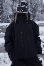 Close-up front view of the all black jacket showing zip pockets and high collar, worn with goggles and beanie
