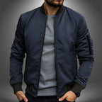 Navy blue bomber-style jacket with ribbed collar, front zip and sleeve zip pocket, worn open over a grey top
