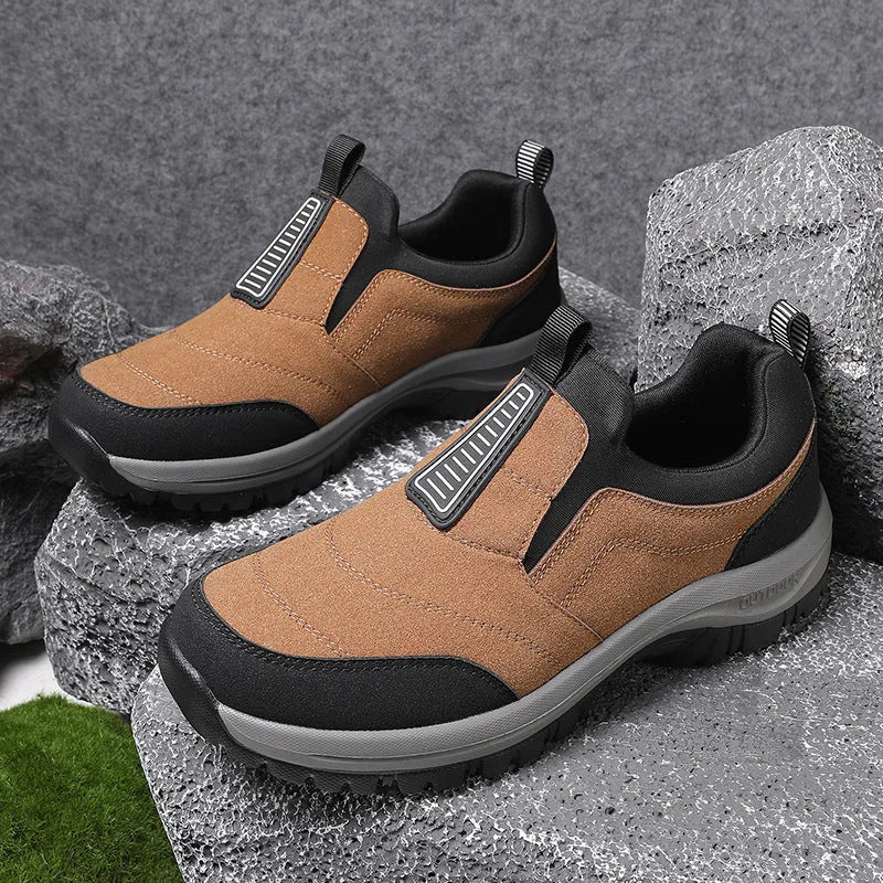 Brown suede-effect slip-on trainer with black overlays and grey lugged sole, angled view on grey rock background