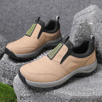 Khaki suede-effect slip-on trainer with black heel panel and grey sole, angled view against stone backdrop