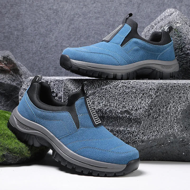 Light grey slip-on trainer with black toe cap and heel, chunky grey outsole, shown on rocky surface