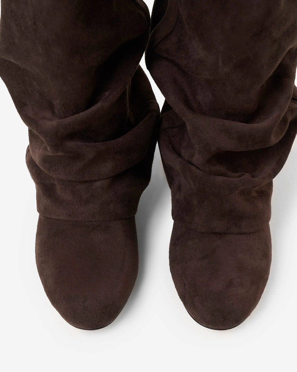 Front view close-up of two slouchy suede boots side by side showing the folded, ruched shaft detail