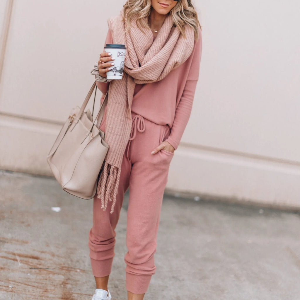 Close-up front view of a woman wearing a soft pink jumper and jogger set with a knitted scarf and beige tote bag
