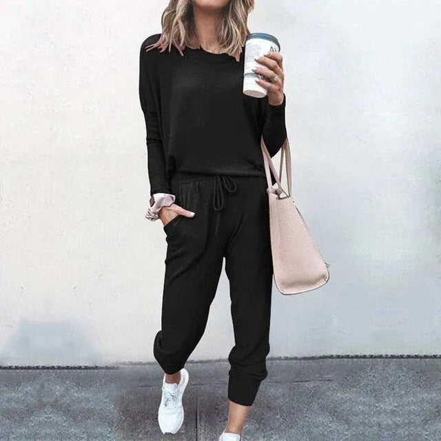 Woman modelling a black long-sleeve top and jogger set with white trainers and a pink handbag
