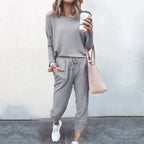 Woman wearing a grey loose-fit top and drawstring jogger tracksuit with white trainers