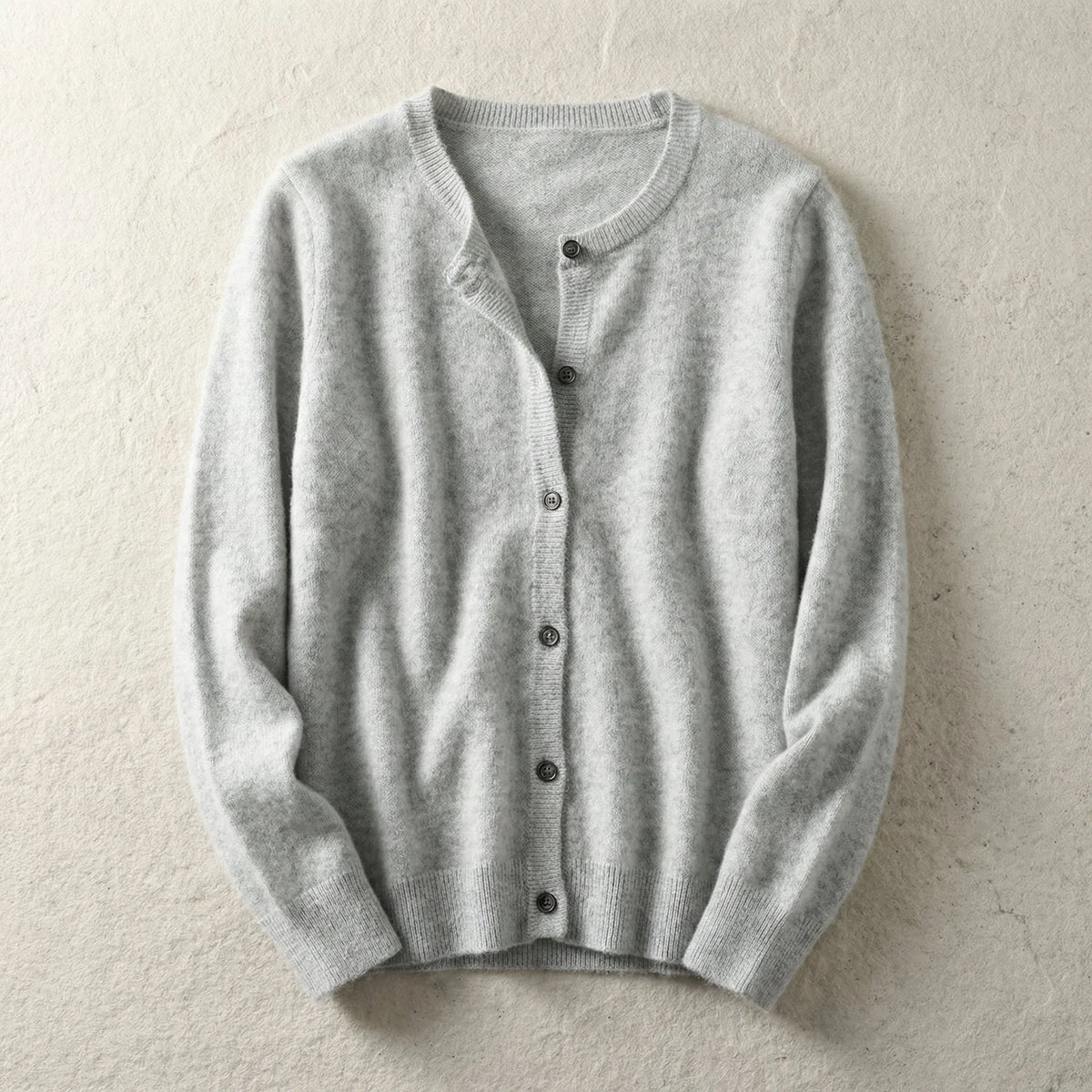 Light grey knitted cardigan laid flat with crew neckline and button front on a textured beige backdrop