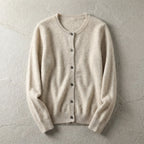 Beige cardigan laid flat showing crew neckline, button front and ribbed cuffs on a textured grey backdrop