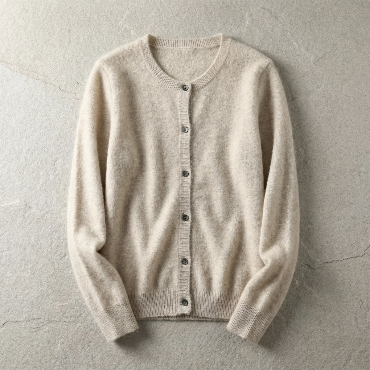 Beige cardigan laid flat showing crew neckline, button front and ribbed cuffs on a textured grey backdrop