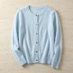 Pale blue cardigan laid flat with full button front and long sleeves on a sandy stone surface