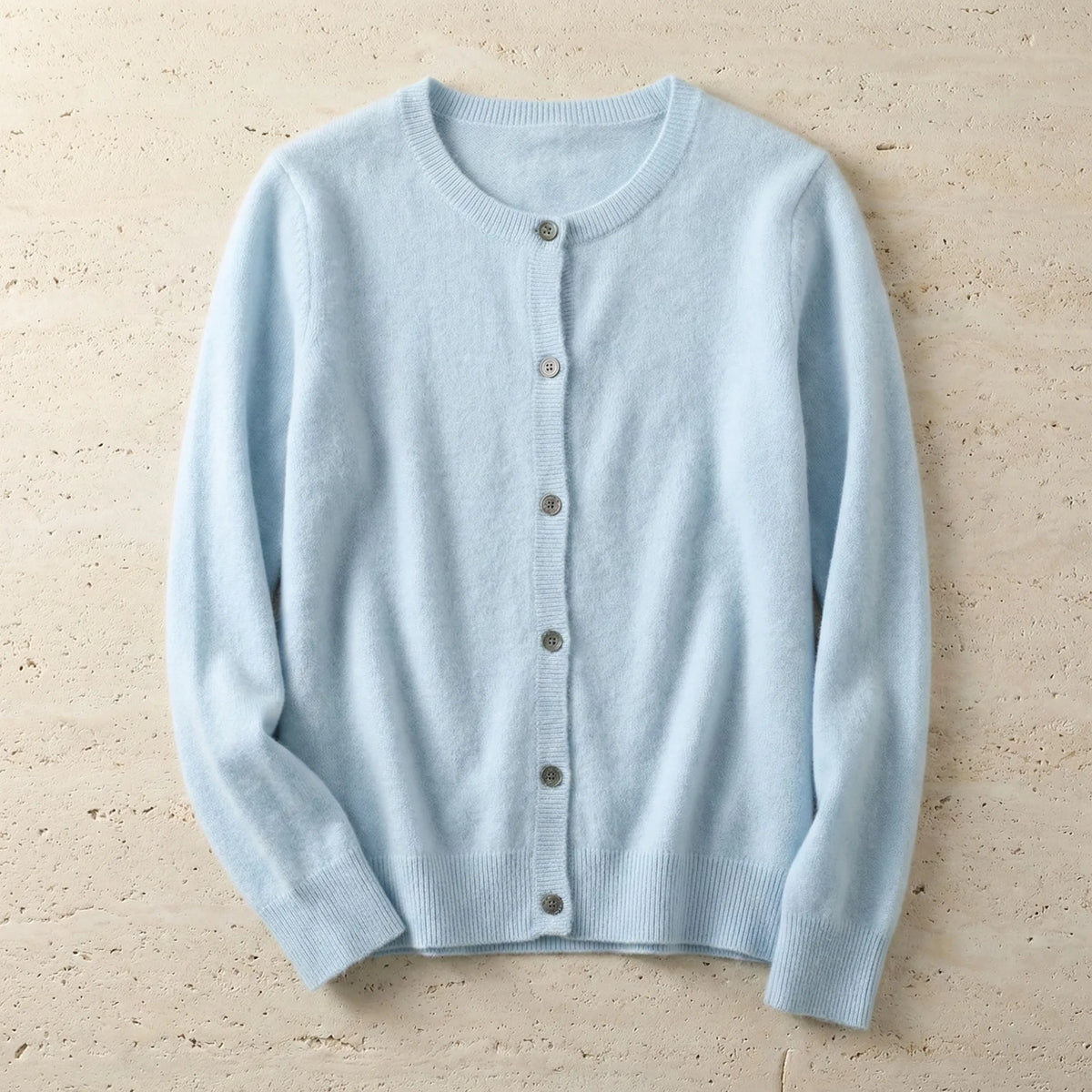 Pale blue cardigan laid flat with full button front and long sleeves on a sandy stone surface
