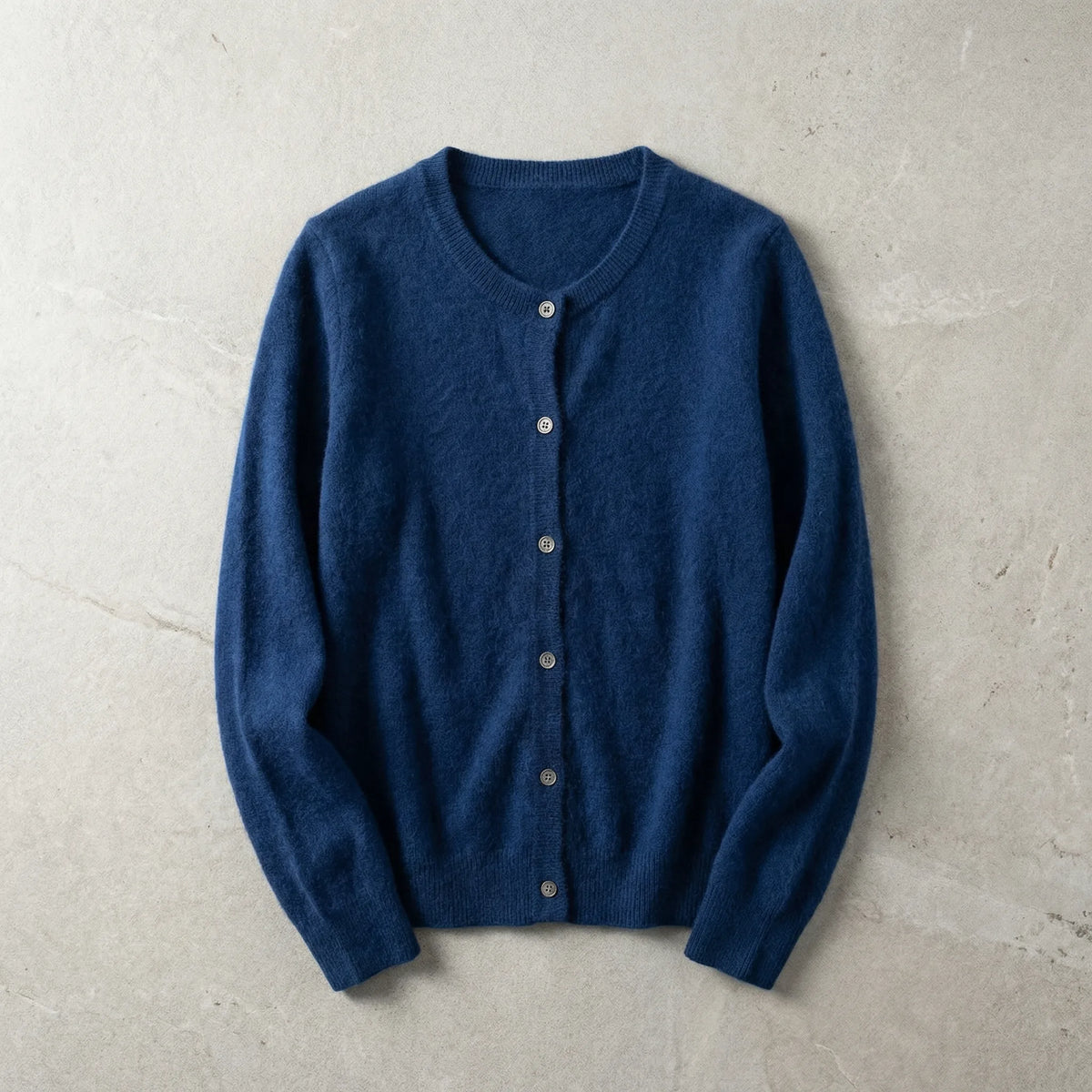Navy blue cardigan laid flat showing crew neck, button placket and ribbed hem on a grey marble backdrop