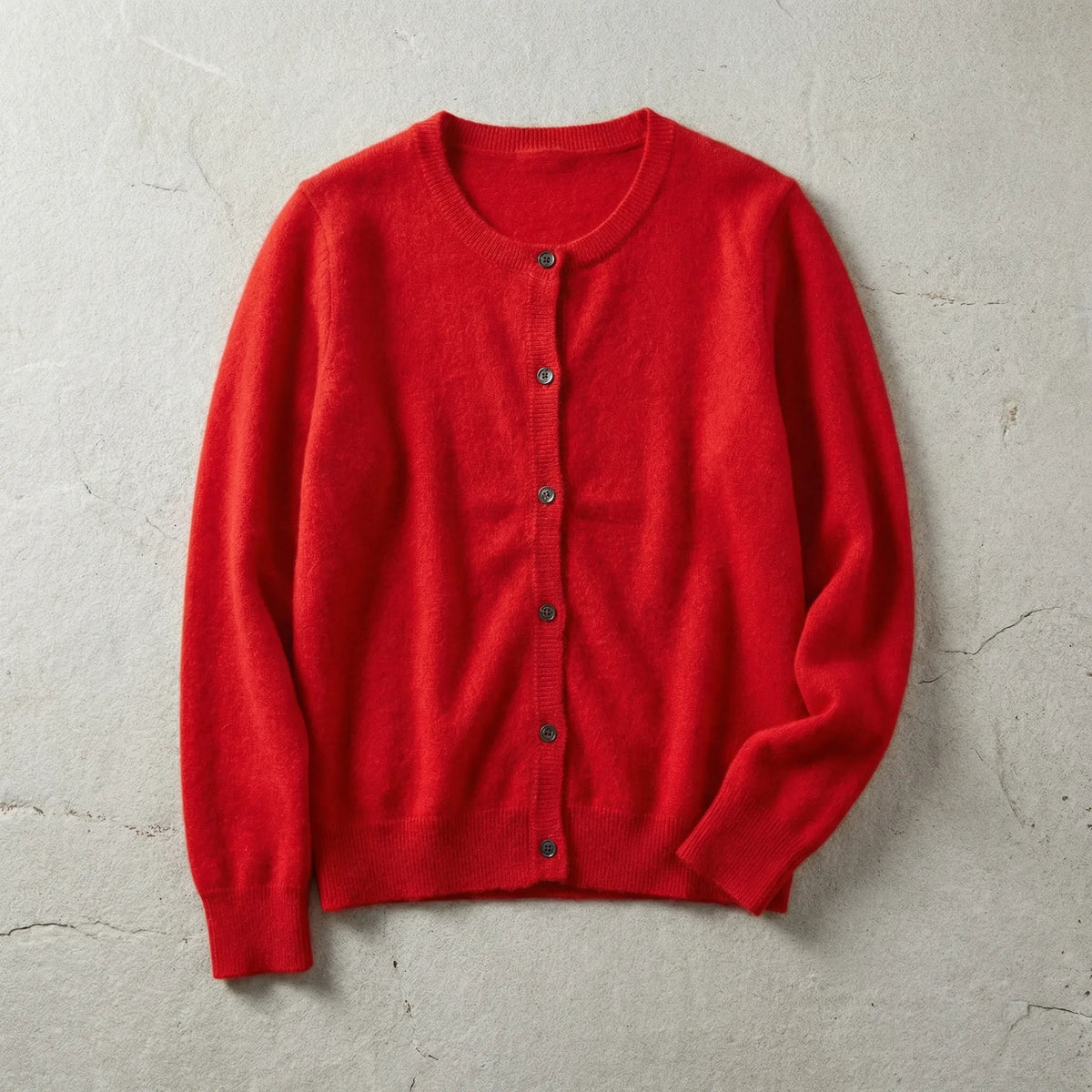 Red cardigan laid flat with button front, long sleeves and ribbed trims on a light grey stone surface