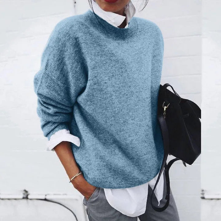 Close-up of a woman wearing a soft blue knit jumper with a mock neck, layered over a white shirt collar.