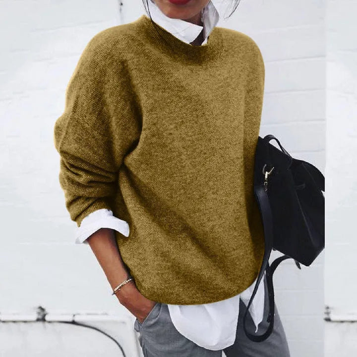 Oversized khaki knit jumper with crew neckline, styled with a white shirt cuff peeking out at the wrist.