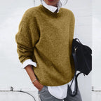 Oversized khaki knit jumper with crew neckline, styled with a white shirt cuff peeking out at the wrist.