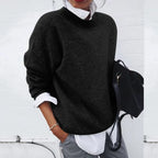 Black knit jumper with a round neckline, worn over a white collared shirt for a smart-casual look.