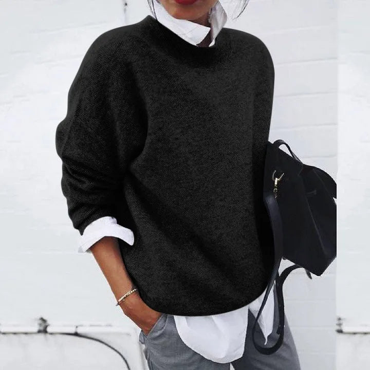 Black knit jumper with a round neckline, worn over a white collared shirt for a smart-casual look.