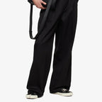 Cropped side view of black wide-leg trousers worn with black split-toe canvas trainers and cream laces