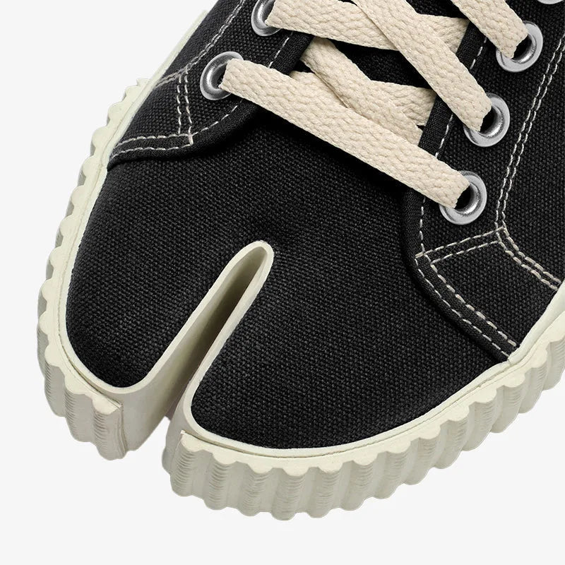 Close-up of the split-toe front showing the tabi-style ribbed sole and contrast white stitching on black canvas