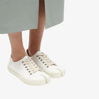 Front three-quarter view of white split-toe canvas trainers with cream laces on a plain background