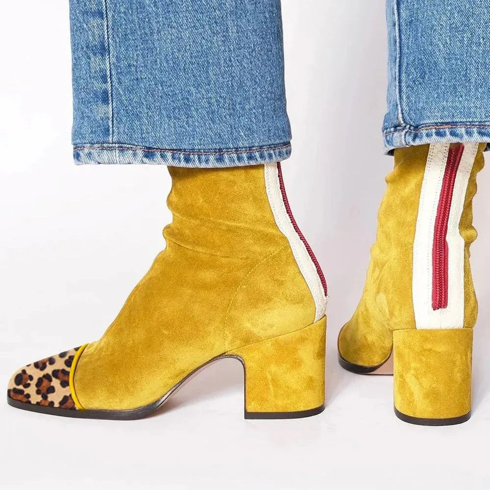 Back view of mustard yellow suede ankle boot with leopard-print toe cap and red zip trim, worn with jeans