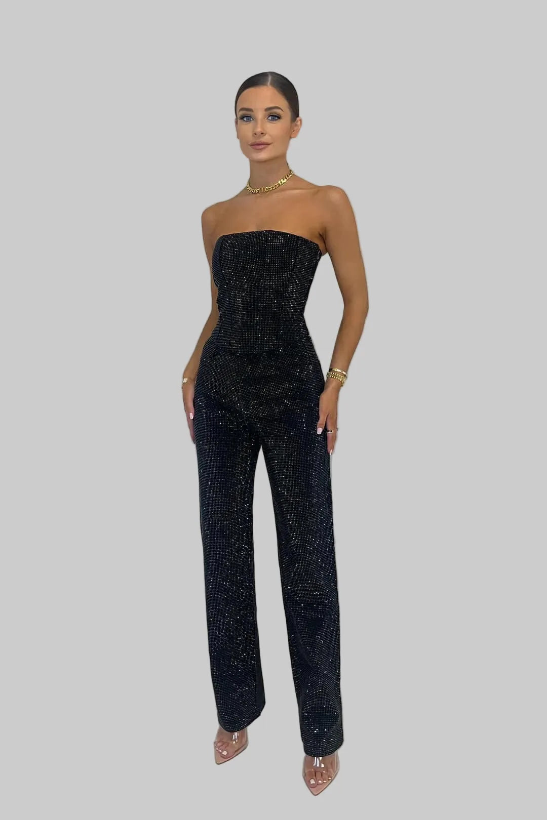 Front view of a woman in a black strapless sequin jumpsuit with straight-leg trousers and a gold choker necklace