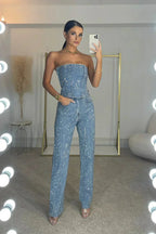 Front view of a strapless sequin denim jumpsuit with corset-style seaming and straight-leg trousers, worn with a phone in hand