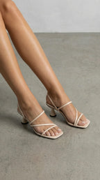 Model wearing beige strappy sandals with crossover front straps and slingback strap