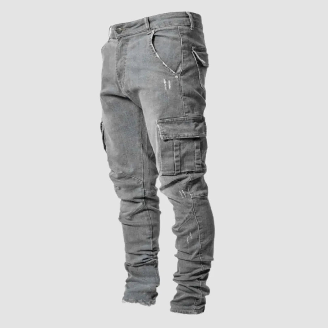 Grey washed denim cargo jeans shown from the side, highlighting the tapered leg and stitched flap pocket.