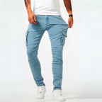 Man wearing light wash denim cargo jeans with white trainers, front view showing the slim tapered leg and side pockets.