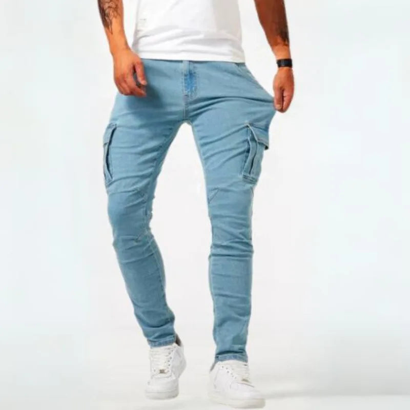 Man wearing light wash denim cargo jeans with white trainers, front view showing the slim tapered leg and side pockets.