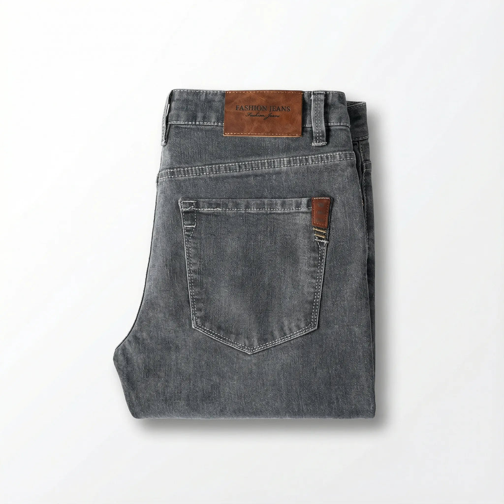 Straight-on view of folded grey jeans highlighting the tan leather waistband label and back pocket