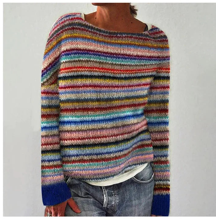 Close-up of a multicolour striped knit jumper with blue ribbed cuffs, worn with jeans against a plain backdrop