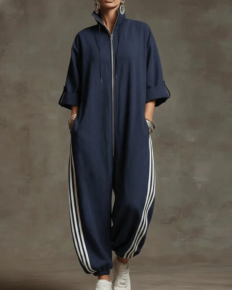 Front view of a woman wearing a dark blue oversized zip-front jumpsuit with striped wide-leg trousers and white trainers