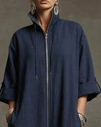 Close-up of the stand collar, silver zip and drawstring detail on a dark blue jumpsuit with rolled cuffs