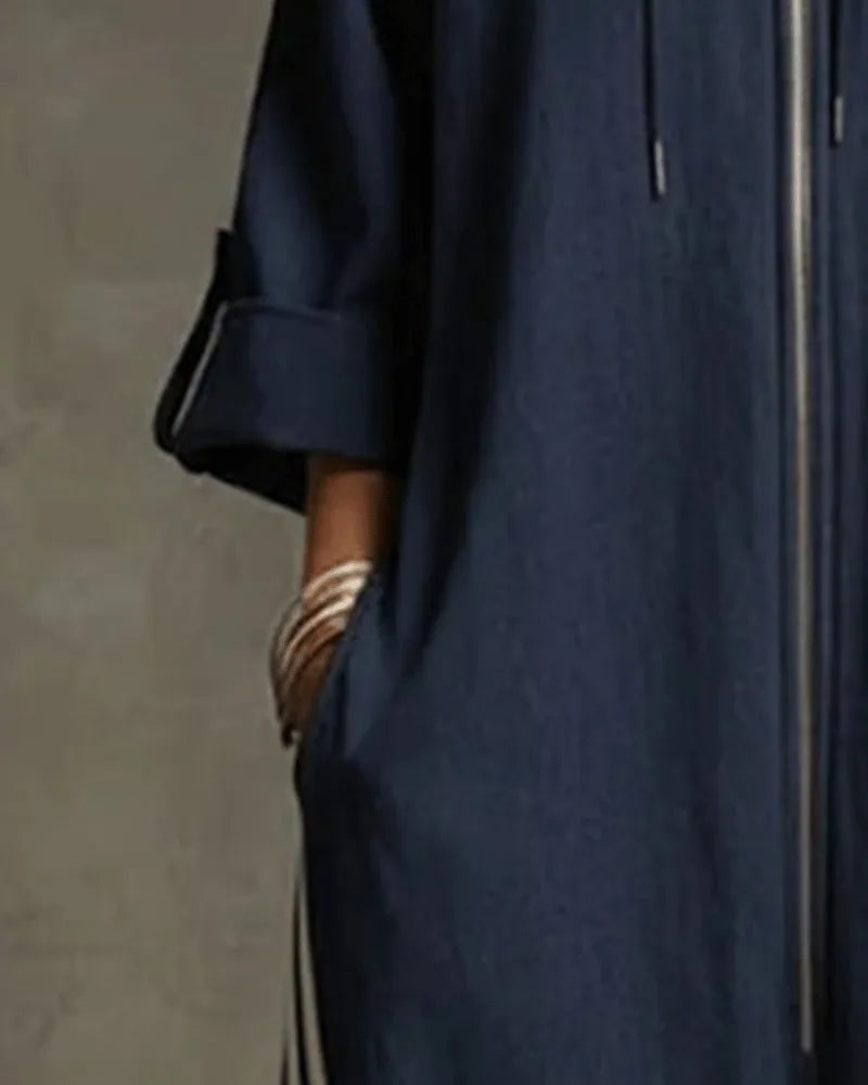 Side view showing the dropped shoulder, rolled sleeve and hand tucked into the front pocket of the dark blue jumpsuit