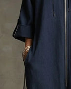Side view showing the dropped shoulder, rolled sleeve and hand tucked into the front pocket of the dark blue jumpsuit