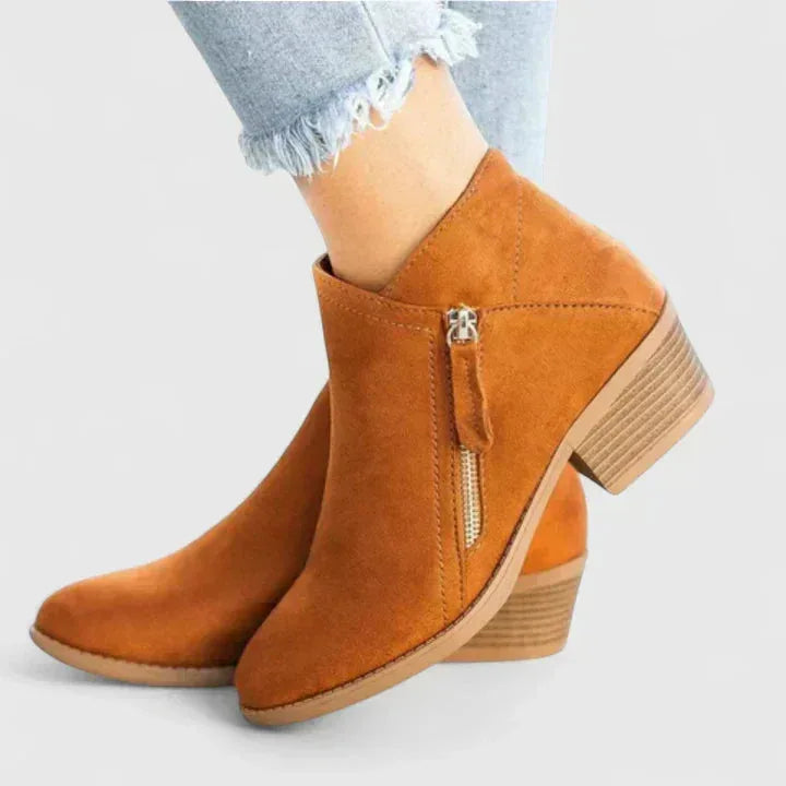 Front angled view of black suede ankle boots worn with ripped jeans, showing zip and toe shape