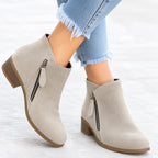 Close-up side angle of red suede ankle boot worn with jeans, showing zip pull and stitched panel