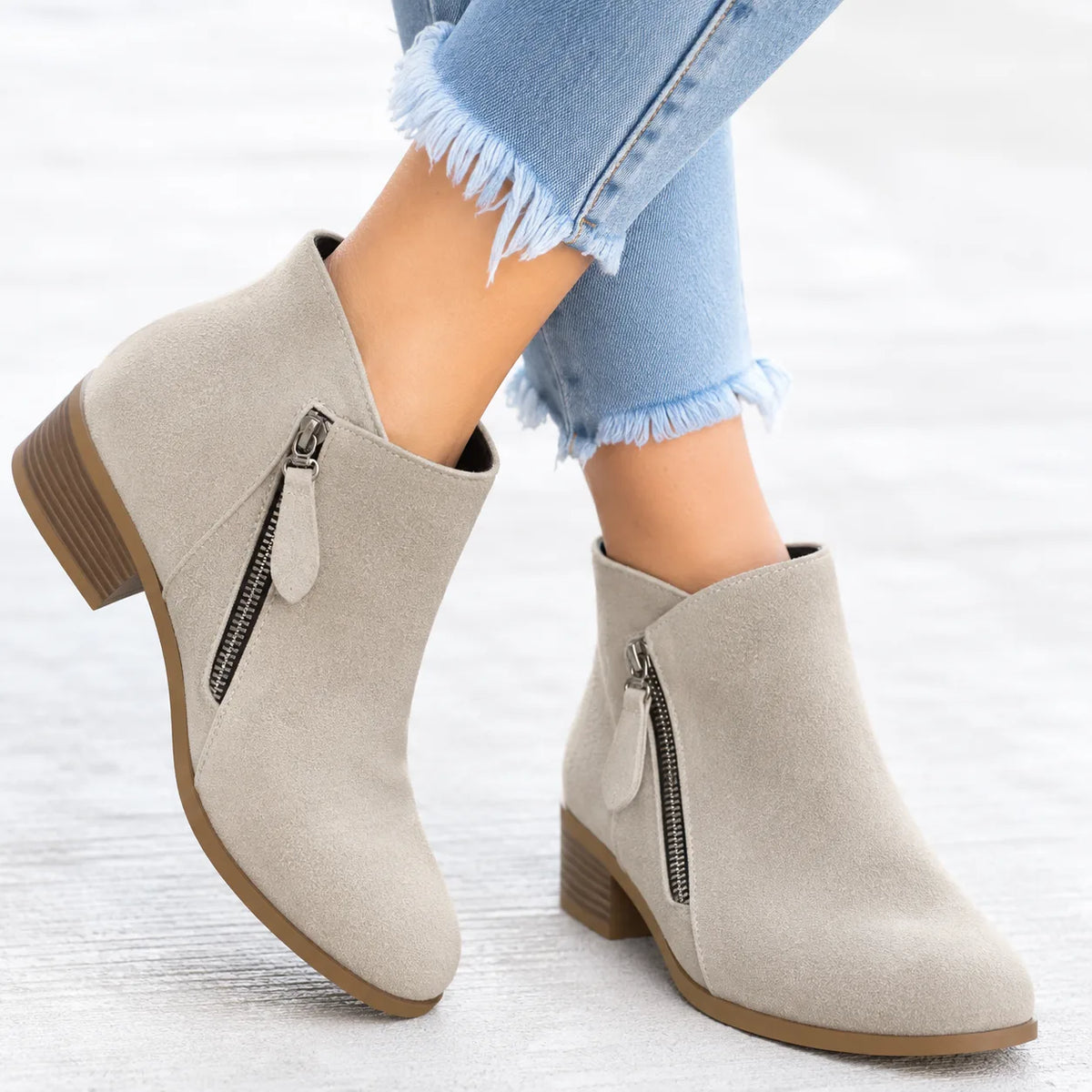 Close-up side angle of red suede ankle boot worn with jeans, showing zip pull and stitched panel