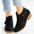 Black suede ankle boots worn with distressed jeans, side profile showing zip pull and low block heel
