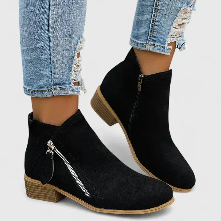 Close-up pair of black suede ankle boots on a plain background showing seam detail and toe shape