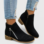 Close-up pair of black suede ankle boots on a plain background showing seam detail and toe shape
