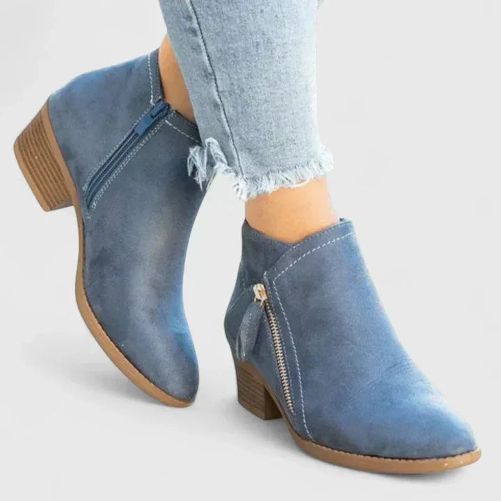 Close-up of blue suede ankle boot worn with jeans, showing the gold-tone zip and stitched seam detail