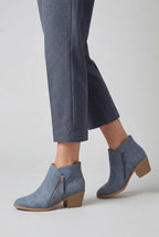 Woman wearing blue suede ankle boots with grey trousers, shown mid-step from the knee down