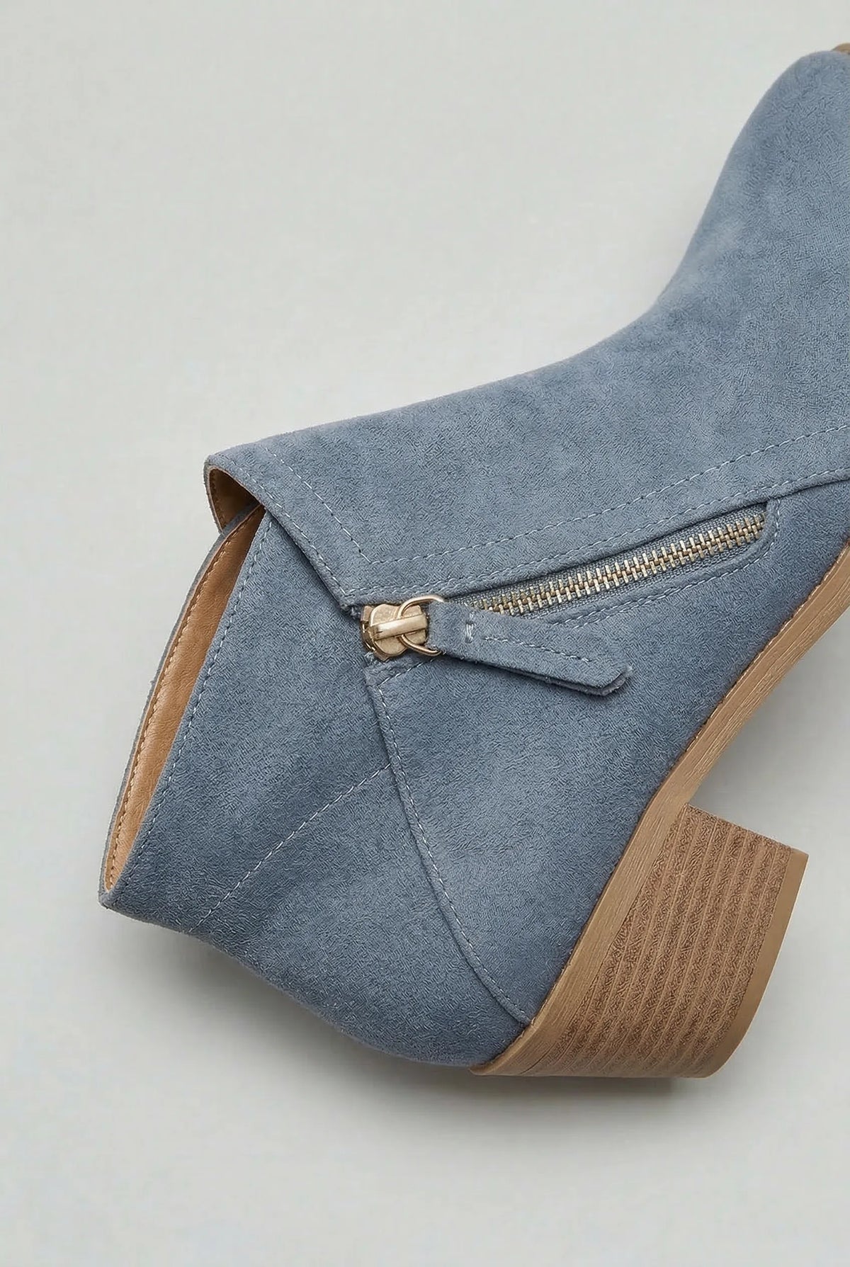 Close-up of the zip pull and stitched seam detail on a blue suede ankle boot heel