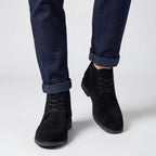 Close-up front view of black suede chukka boots worn with rolled navy jeans, laced front detail visible